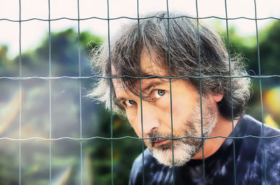 Close-up portrait of young man against blurred fence