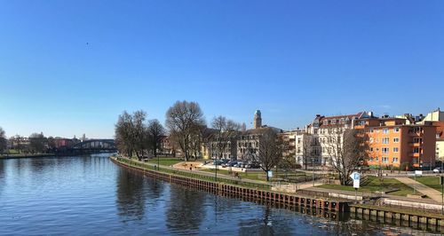 Canal in town against clear blue sky