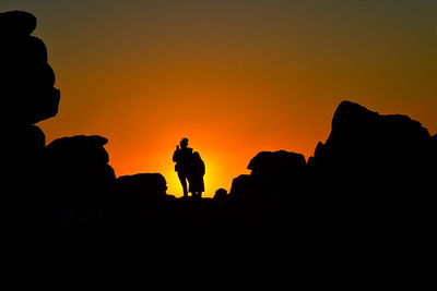 Silhouette people on rock against sky during sunset