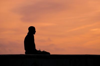 Silhouette of person sitting against sky