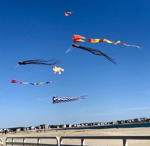 Low angle view of kites flying at beach against blue sky