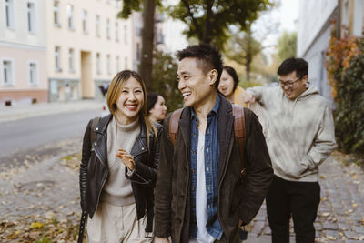 Male and female friends laughing while walking on sidewalk