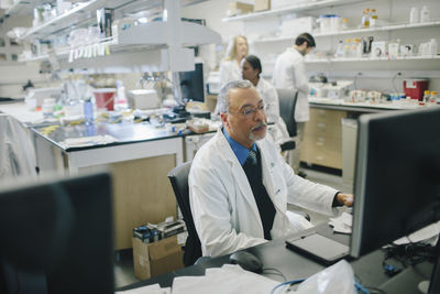 Male doctor using desktop computer while coworkers working in background at hospital