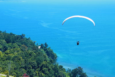 People paragliding over sea against trees