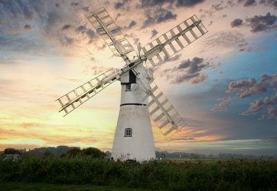 Traditional windmill on field against sky during sunset