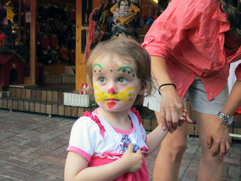 Cute girl with painted face holding mother hand on footpath