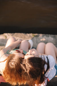 Happy lesbian couple sitting by river in city during summer