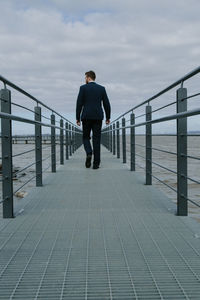 Rear view of man walking on pier over sea against sky