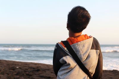 Rear view of man standing on beach against clear sky