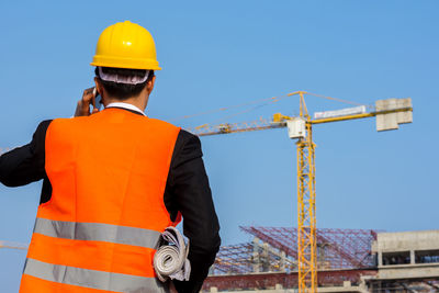 Rear view of engineer using phone at construction site against clear sky