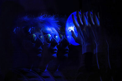 Multiple image of man holding illuminated blue light in darkroom