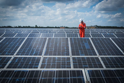 Engineer standing amidst solar panel against cloudy sky