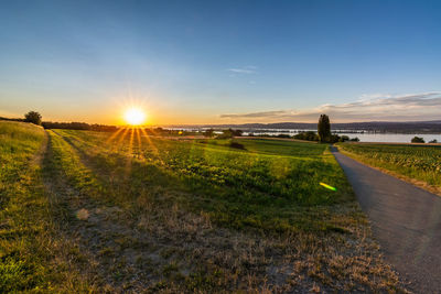 Road amidst field against sky during sunset