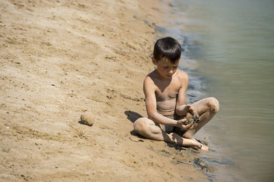 Playful shirtless boy sitting on shore at beach