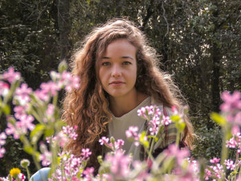 Portrait of young woman sitting by trees and plants at park