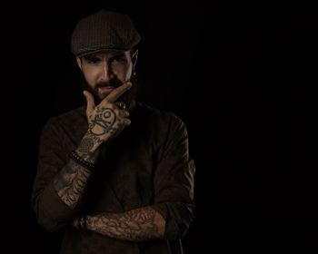 Portrait of young man with tattoo standing against black background