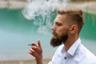 Concept. smoke enveloped man head against backdrop of reservoir in park.