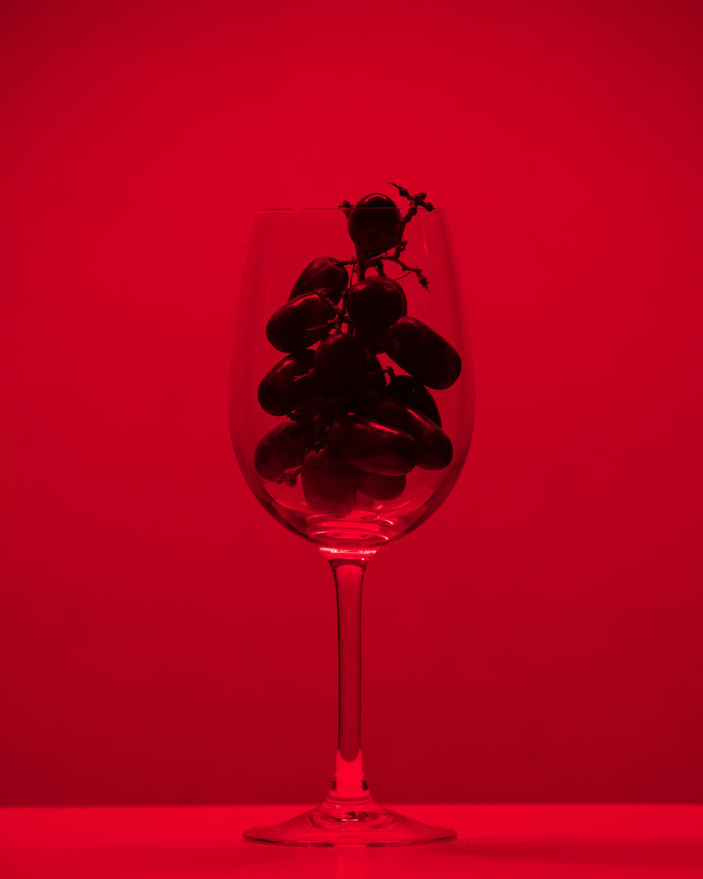 CLOSE-UP OF WINE GLASS ON RED TABLE AGAINST ORANGE BACKGROUND