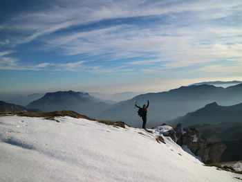 Woman with arms raised standing on mountain against sky