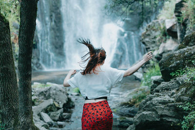 Rear view of woman standing against waterfall