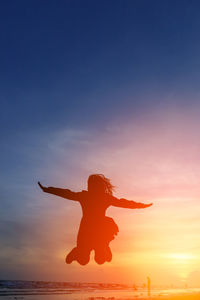 Silhouette man jumping on beach against sky during sunset