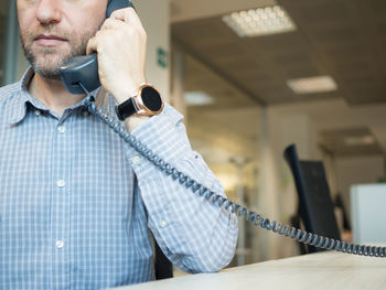 Midsection of businessman talking on landline phone at office