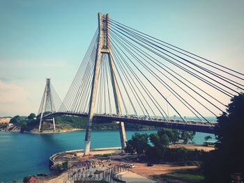 Suspension bridge over river in city against sky