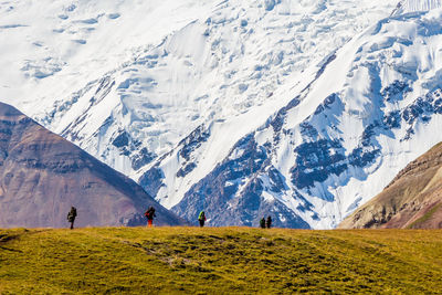 Hikers on landscape against snowcapped mountain