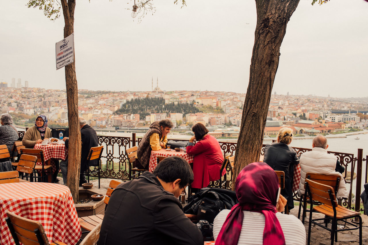 REAR VIEW OF PEOPLE SITTING AT TABLE IN CITY