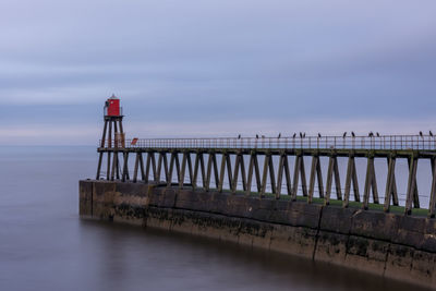 Lighthouse and pier in sea against sky