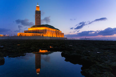 Lighthouse by building against sky during sunset