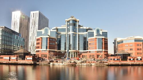 Buildings by river against sky in city