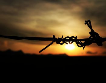 Close-up of silhouette barbed wire against sky at sunset