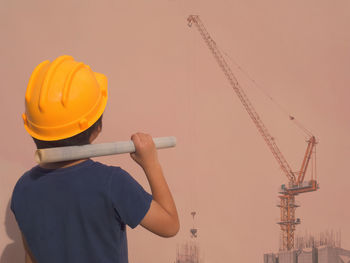 Rear view of architect holding blueprint standing at construction site