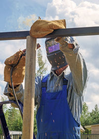 Man welder in a welding mask, construction uniform protective gloves cooks metal on  site.