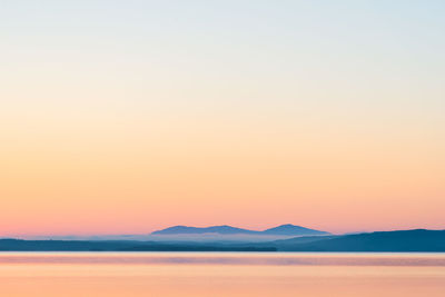 Scenic view of sea against mountains and clear sky during sunset