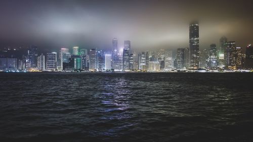 Illuminated cityscape in front of sea against sky