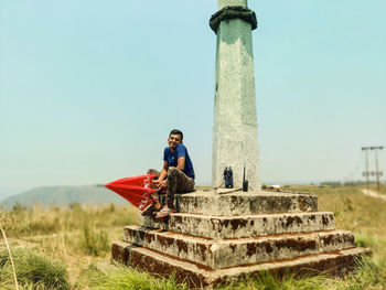 Man sitting on column against clear sky