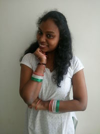 Portrait of smiling young woman wearing tricolor bangles standing against wall