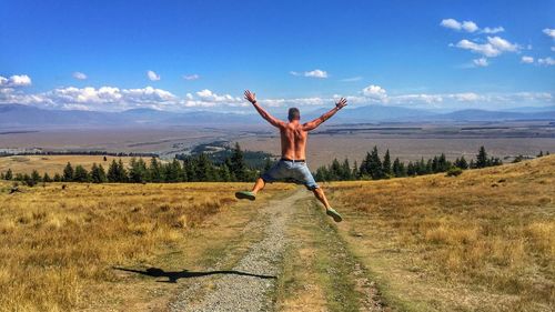 Rear view of shirtless young man jumping on field against blue sky