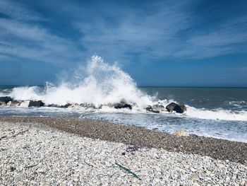 Waves splashing on rocks at beach against sky