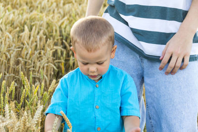 A happy little boy and his teenage brother are walking in a wheat field on a bright, sunny day.