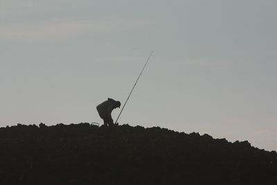 Low angle view of silhouette man fishing against clear sky