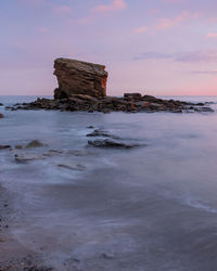 Rock formation on beach against sky during sunset