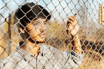Portrait of young man seen through chainlink fence