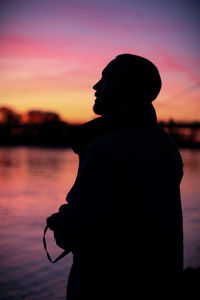 Silhouette couple standing by sea against sky during sunset