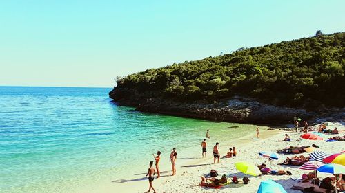 People at beach against clear blue sky