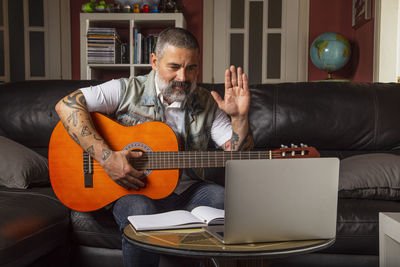 Man playing guitar on sofa at home