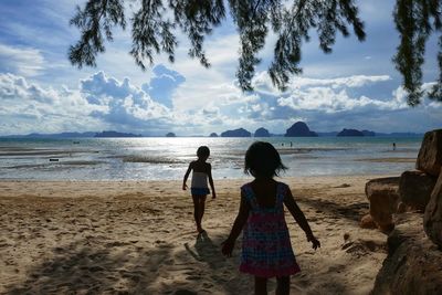 Rear view of children walking at beach against sky