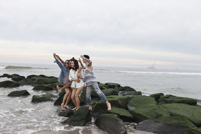 People on rock at beach against sky